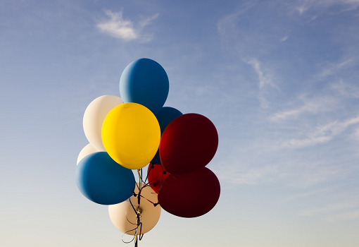 Red, yellow, cream and blue balloons in blue sky with clouds