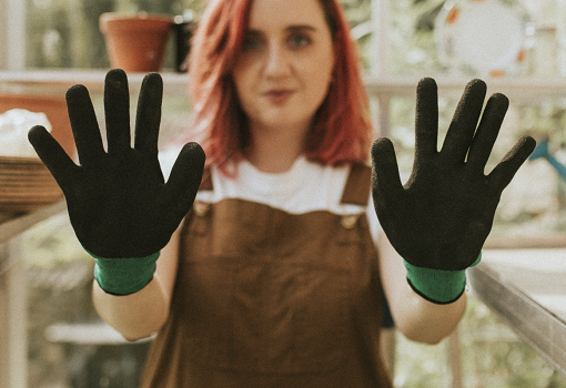 Young woman in brown apron wearing black and green gardening gloves, holding hands up