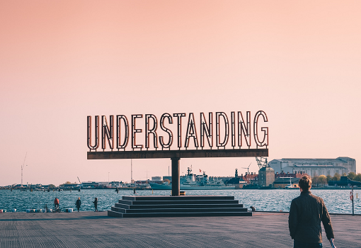 Sign by water which reads 'Understanding', with pink sky background