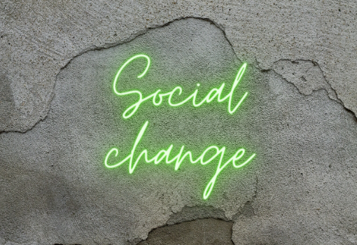 Neon green sign on grey wall saying 'social change'.