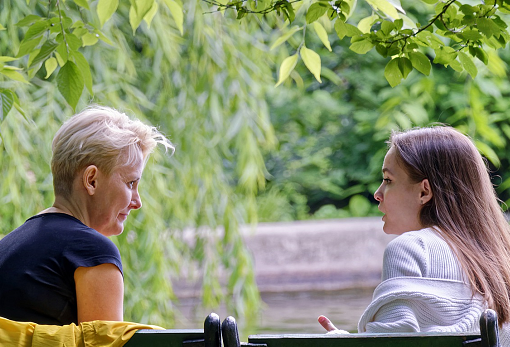 Young person talking to woman on bench next to tree