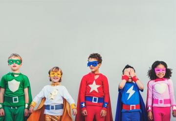 Children standing in a line against a wall, wearing superhero costumes
