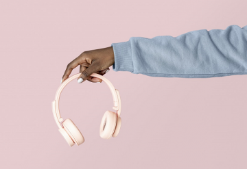 Hand in grey sweatshirt holding pink headphones on pink background