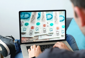 Man looking at laptop screen with £5 and £10 notes